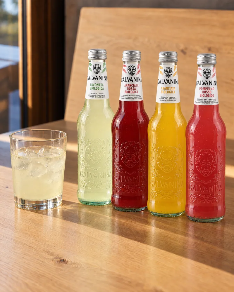 Four bottles of Galvanina beside a glass of lemonade