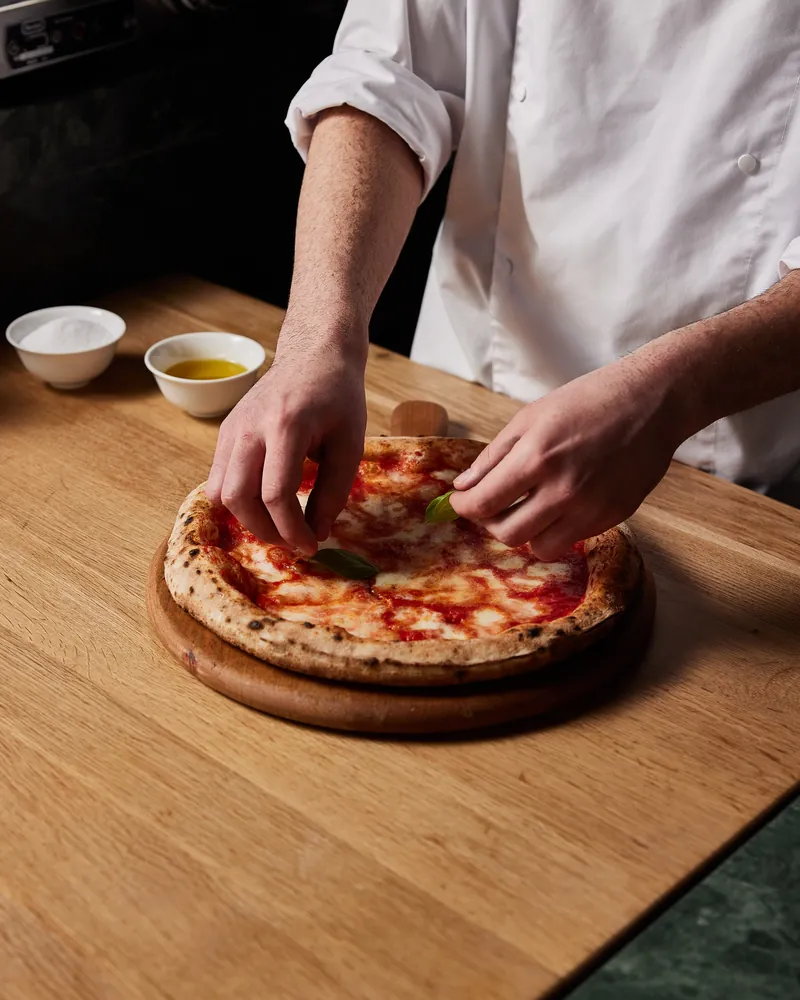 Hands finishing a pizza on the board