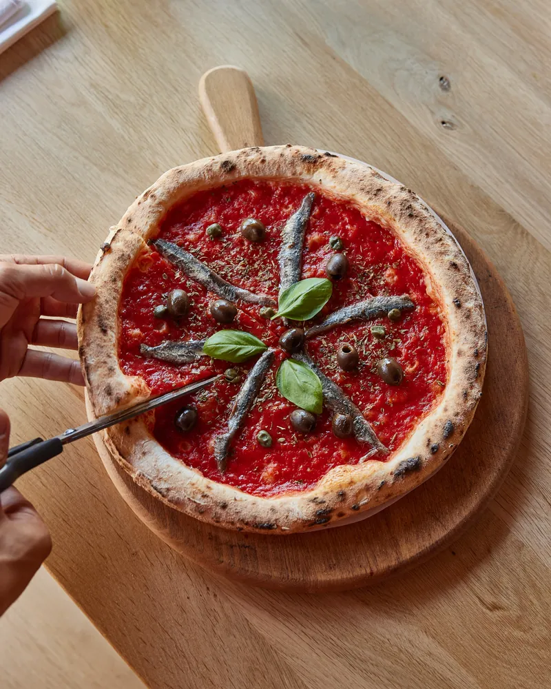 A pizza with anchovies cut at the table