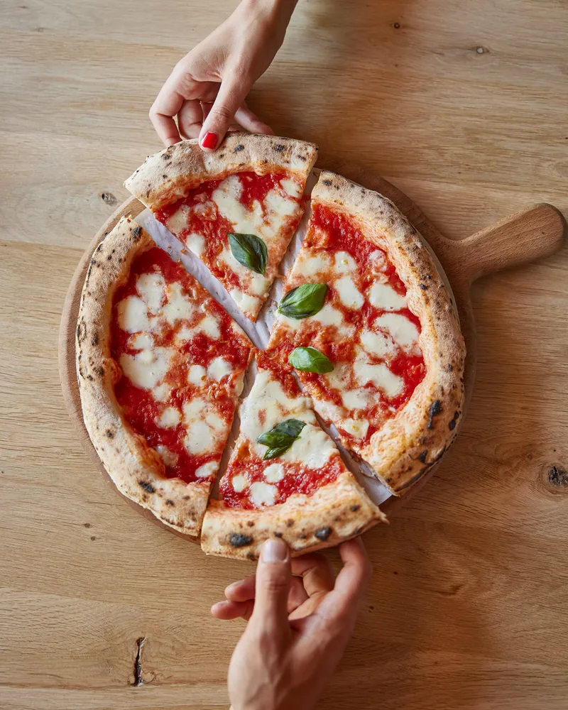 Two hands pulling apart a cut Margherita